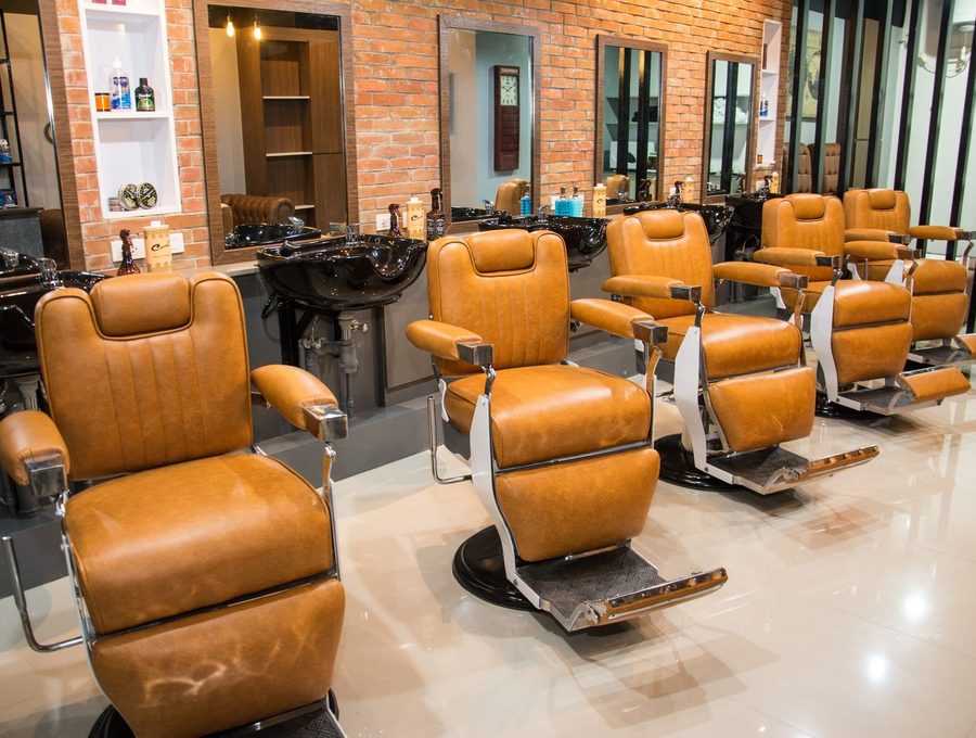 A row of tan leather barber chairs against a brick wall