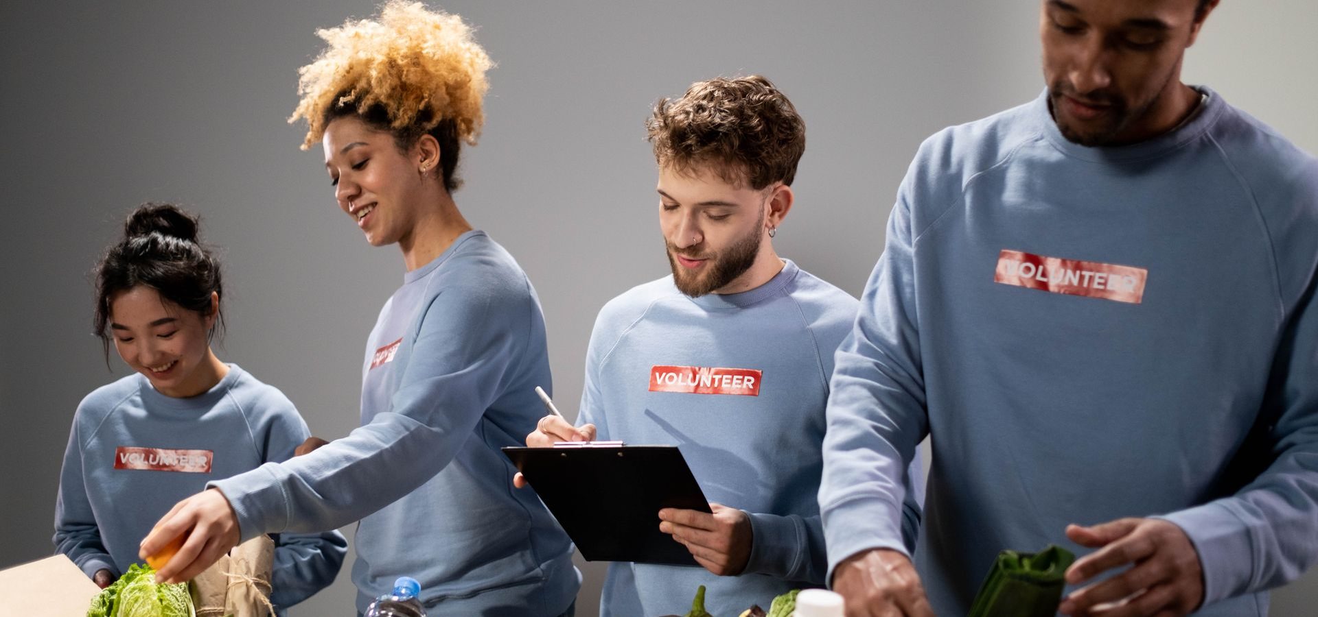 Four volunteers in matching sweatshirts sorting food donations at a table