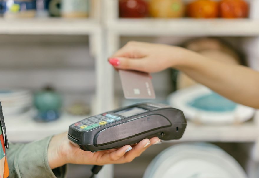 A shop assistant holding out a handheld card terminal as a customer taps a card