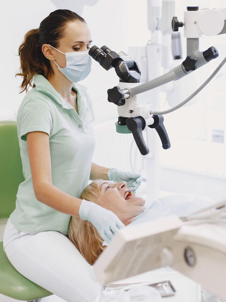 A clinician working with a dental microscope beside a patient