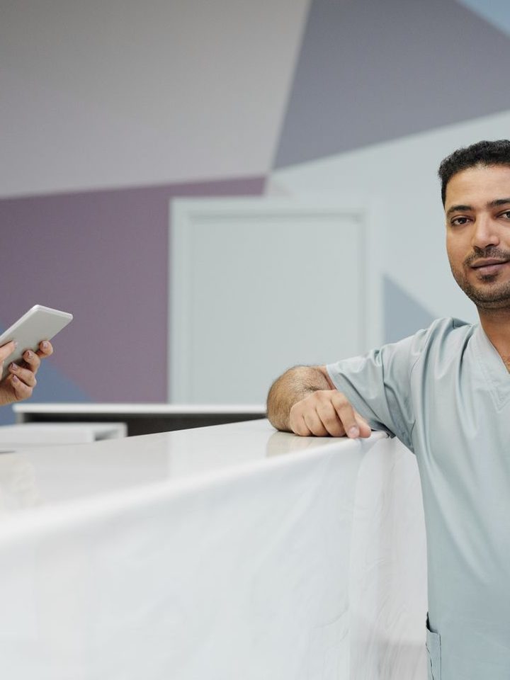 Two clinicians in scrubs at a practice front desk with a tablet