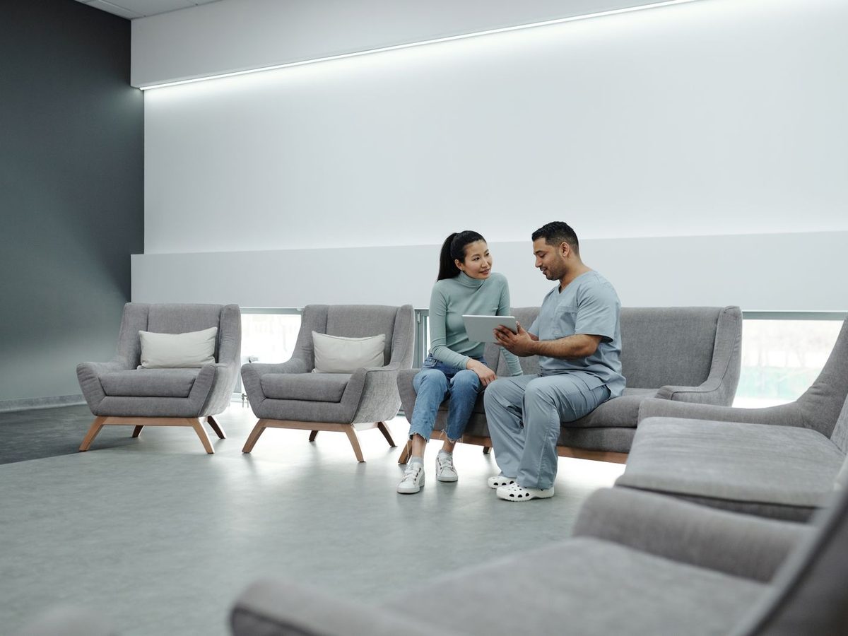 A clinician and a patient sitting together in a bright waiting area, reviewing a treatment plan on a tablet